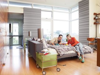 Koshkarian and DiFrancesco lounge on their Poliform bed with their daughter, Zia. The large windows annex an outdoor patio, which extends the already light-filled space into the outdoors.