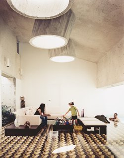 Three protruding concrete skylights brighten this living room, despite the graphic floor tile and dark ceiling.