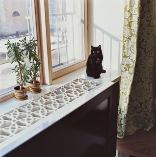 Moby the cat sits on the windowsill, which the architect constructed by cutting a geometric pattern into a thick sheet of MDF, a fiberboard product that’s inexpensive, easy to machine, and unrecognizable when coated in white lacquer paint.