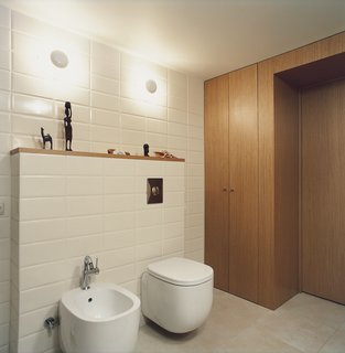 In the bathroom, which is tucked under the mezzanine, the toilet-bidet set from Pozzi Ginori boasts rounded rectangles with pleasingly deep but minimal basins. The wall sconces are from the Spanish lighting company Vibia, and fit neatly between brick-like rectangular tiles.