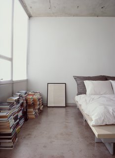 Who needs shelves when there's plenty of floor space? Stacks of books and a framed print sit alongside a Peter Maly Ligne Roset bed, reupholstered in stiff linen.