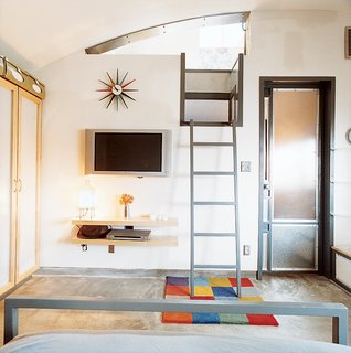 A ladder leads up to the bedroom, which is tucked under the curve of the vaulted roof. The Sunburst clock is by George Nelson; the flat-screen TV is by Philips.