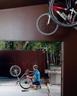 Venetian Vicissitude - Photo 7 of 9 - Pierre Kozely mends his bike on a patio in the rear yard, seen from their garage—which was transformed into a media room. Behind him is a Cor-Ten rolling gate that gives access <br><br>to the back alley.