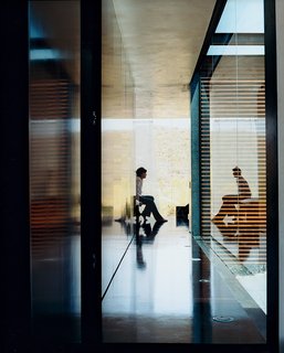 The hallway leading to the sparsely furnished bedroom opens to a wall of glass, where the light reflects off the dark NAP board floors and walls. The lighter walls are thin-coat gypsum plaster with a beeswax coating.