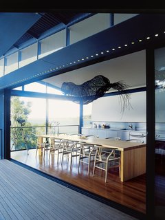 Three Glass-and-Copper Pavilions Conquer the Cliffs - Photo 5 of 10 - Caroline Casey designed the curving dining table, which is surrounded by Hans Wegner's Wishbone chairs. Suspended over the table is an old Aboriginal fishing trap.