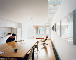 Kim reads the newspaper in the all-white kitchen. White paint, which requires fewer coats than color, was a money-saving strategy. The desk chairs and aluminum lounge chair are both Eames, courtesy of Fernandez’s scavenging.