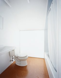 Upstairs, simple porcelain pieces such as a Kohler toilet adorn the modest master <br><br>bathroom. Beneath the downward-pitched ceiling, a polycarbonate-panel wall brings in light from the south-facing skylight behind.