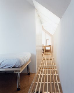 An ingenious floor treatment—slats laid over the ceiling beams—enables the skylight to do double duty, pouring sunlight into the living room below. The translucent bathroom wall turns that into triple duty.