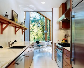 The Pace of Portland - Photo 3 of 6 - To brighten the kitchen, which was once the darkest room, Watson and Tschopp decided on a glossy white finish, painted directly on the same rough-cut cedar paneling used throughout the house. This maintains the consistency of materials and texture, while reflecting light and enhancing the natural illumination. Stainless steel appliances and vintage bronze hardware add luster. Super White semigloss (walls) and Old Pick Up Blue (ceilings) are by Benjamin Moore.