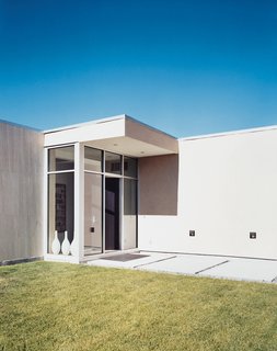 A meticulously manicured lawn complements the pared-down lines and massive front door. At night, the path to the door is illuminated by floodlights.