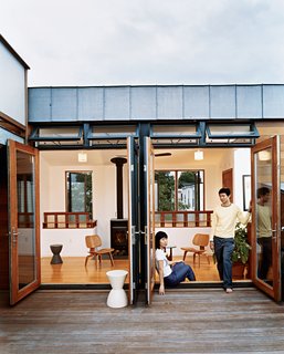 Jinhee Park and John Hong, in a doorway that opens to the building’s shared roof deck. Behind them is the upstairs lounge of their neighbors, adorned with Eames chairs, Kartell stools, and a woodstove from Rais Wittus.