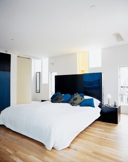The narrow windows flood the master bedroom with light, while providing privacy. The dark-stained woods of the custom headboard and nightstands, all designed by the architect and built by Solicraft, cohesively tie the furnishings to elements like the bedroom sliding door and exterior concrete paneling.