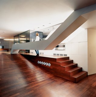 The Penthouse Has Landed - Photo 14 of 16 - The long floating counter is a sculptural element that continues the line of duct-like exterior elements. The sloping floors are made from a rich-looking African cherry wood called Doussie. The metal disks beside the ramp are smoke and heat vents. The architects aimed to create an interior without any barriers or columns in order to have an uninterrupted spatial continuum. They appear to have succeeded in their efforts.