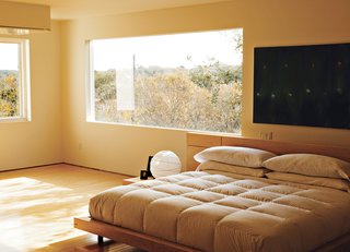 In the third-floor bedroom, horizontal wood-framed casement windows by Pella open out to tree-filled views of Lake Austin and Westlake Hills. Comfortably austere, the only furniture here is the bed, two nightstands, and a marble table for books and candles. Erik designed the bed, nightstands, and marble table; the paintings are by Jair.