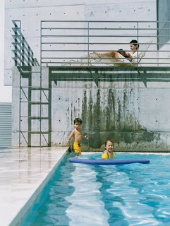 The kids and their mother relax in the pool area, their figures framed against a monochromatic background of steel and concrete.
