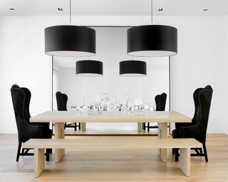 The kitchen opens up to the dining room, where Hollis played with size and shape. She designed the solid French oak dining table and bench, which were fabricated by B Serota Furniture and Architectural Design, and flanked the table with a Host and Hostess chair from Coup d'Etat San Francisco. She hung two Piet Boon-designed drum pendants over the table and placed a large mirror on the wall to extend the space so that the person sitting on the bench can see the living room fireplace in the reflection.Photo by <br><br>Ben Mayorga Photography