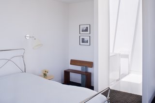 Back in the master bedroom, the designers installed Tolomeo wall sconces by Artemide next to the bed and placed a bench next to the door made by Hart's uncle, Peter Czuk of Czuk Studio. The bedroom door, which is rarely closed, is the starting point for the continuous flow of movement and light from the top of the house to the main level and down to the bottom floor.<br><br>Photo by <br><br>Sharon Risedorph