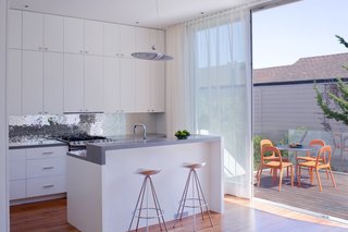Grist and Goldberg wanted an open kitchen so their guests could gather around a beautiful space without feeling cramped in a tiny room. Goldberg instantly fell in love with an Ann Sacks glass tile backsplash that Samaha and Hart showed the couple during the design process, but she wasn't willing to spend $100 per square foot on the product. Instead, Goldberg had their contractor make three panels of cement board that would fit in the backsplash space and she and a friend spent their evenings gluing on glass tiles that she purchased online. When they finished, the contractor came back, installed the panels, and Goldberg filled in the gaps. Outside, chairs from Ikea and an Inox table from DWR provide a space to sit on the deck.<br><br>Photo by <br><br>Sharon Risedorph