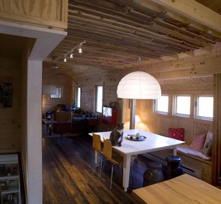 The ceiling was dropped over the dining room to provide a more intimate setting. Strips of salvaged hemlock and chestnut wrap the interior wall and ceiling. A loft for naps and overnight guests is above. Image courtesy Chad Everhart Architect.