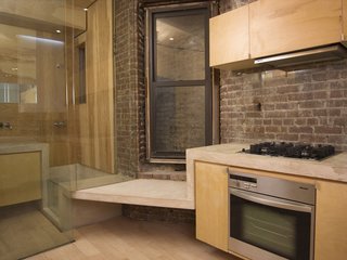 The kitchen has a Miele cooktop, oven and hood, as well as a small seat before a double-hung window, one of very few natural light sources in the apartment. The concrete ribbon continues into the adjacent bathroom, becoming part of the bathtub and counter. Image courtesy Brian Riley.