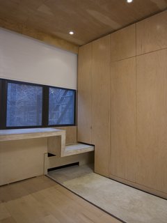 Floor-to-ceiling maple sheathes the storage cabinets and the bottom of the Murphy bed, at right. The concrete ribbon continues as a window seat before becoming a desk.