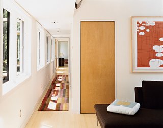 A view from the top of the stairs, past the office to the master bedroom. Sunlight filters through extensive fenestration to the hall, which features a runner by Emma Gardner. Artwork by Campbell Laird hangs over B&B Italia seating in the couple’s office. Not shown is a Herman Miller desk complete with Aeron work chair.