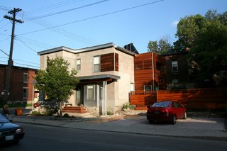 The home’s entrance is located just around the corner from the confectionary entrance. The bay window form is original, but was modernized with a concrete exterior. At right, housed in mostly reclaimed cedar, is the portion containing the upstairs deck. A new fence encloses the small, previously exposed yard.