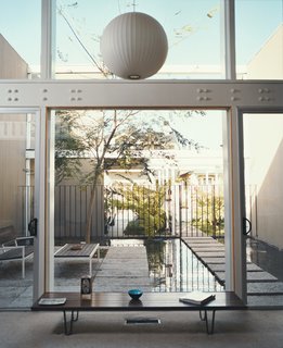 The double-height living space looks out to the reflecting pool and entry. A George Nelson Bubble Lamp, Edward Wormley Long John Bench, and Van Keppel Green settee and table were among the home’s original furnishings.