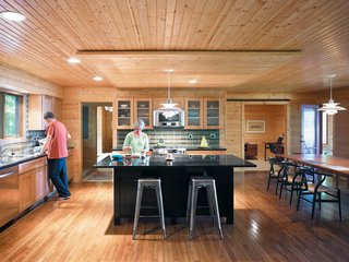 Campbells' Coup - Photo 10 of 12 - In the kitchen, Danish PH 5 lamps illuminate the island and table. The lined wood planks on both the ceiling and floor draw the eye naturally through the space to the study beyond, where Keith’s father’s original Jens Risom desk resides.