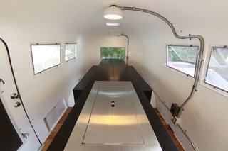 To maximize the small space inside the Airstream, Suzuki removed the existing structures and added a central island the follows his kenchikukagu style of design. Near the door (front of photo), a sink and cook top is hidden under the steel cover. At the rear (back of the photo), a dining table transforms into a set of twin beds. Photo by Sadamu Saito.