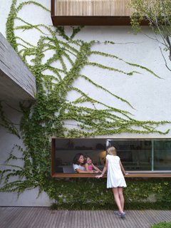 From the garden deck, Sophia Cóser talks to sister Helena and mother Piti through a wide, low-slung window typical of architect Marcio Kogan.
