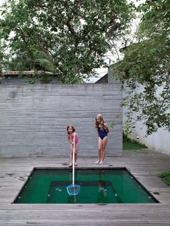 Sophia supervises her sister Helena as she cleans the surface of the small pool, whose rich emerald tiles echo the luxuriant greens of the garden’s tropical plantings.
