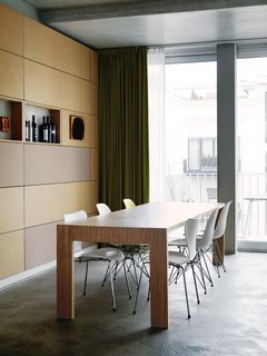 Next to the kitchen, Eames and Jacobsen chairs welcome dinner guests to the dining-room table. The back wall is covered in particleboard panels.