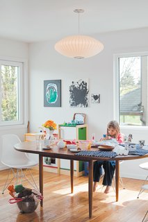 Daughter Zoë finds a cozy spot at the dining-room table, by Dux, seated on an Eames Molded Plastic chair and under a George Nelson Saucer lamp.