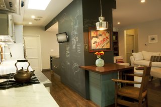 Architectural designers Chinmaya Misra and Apurva Pande retained the existing structural fireplace wall inside, now sheathed in useful chalkboard paneling, then knocked down a light-blocking wall between the living area and the kitchen and introduced new millwork and appliances to the space. The door at left leads to the garage; at right is the door to the couple’s former bedroom.
