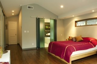 The ceiling of the new master bedroom follows the gable pitch of its barn-inspired roof. The white door leads back into Lyall’s study; more sliding glass doors lead to the remodeled master bath. The horizontal sliver window at right allows views of the treetops and lets breezes in, yet retains privacy.