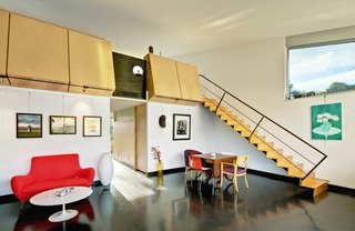 Wong’s photographs dot the living area/studio; a painting by Li is at right. The architects put in a black concrete floor and designed the overhead birch-ply blocks, which double as bookcases for the upstairs sleeping loft. Accompanying a Saarinen Tulip table is a loveseat from Palazetti. Architect Michael Graves designed the chair with the circular cutout; opposite it is one designed by architect Jim Wallace for Novikoff, and the pair of red-and-white Catifa chairs are from Arper. The stair is made from Radiata plywood.