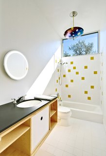 Light floods the second-floor bath, which is housed within a birch-ply "box" also containing storage. The water is heated by a tankless, on-demand unit from Rinnai. The architects continued the tile motif for the bath downstairs; the honey-colored tiles are from Dal-Tile. The lamp is by Kathleen Ash of Studio K Glass.