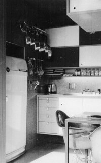 The refrigerator is tucked in the void under the stair, making the kitchen more a composition of furniture than appliances.