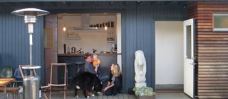 Shoup, his wife, Taya, and daughter, Hannah, relax on the deck off the kitchen with their dog, Stella. "For a high percentage of the year, we just roll open the door, and everybody hangs out in the kitchen, where we can keep an eye on Hannah," explains Shoup. "There’s kind of a leathery quality to it," he says of the door, which he fabricated of steel, with glass salvaged from an old sliding door. The sandstone sculpture is called "Mother and Daughter." Photo by Aya Brackett.