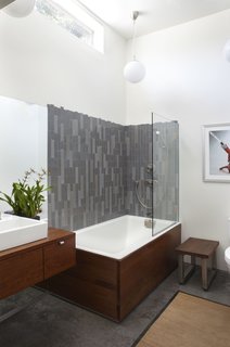 Shoup accentuated the feeling of space in the master bath by opening it up to the full ceiling height. Ipe wood sheathes the sink and tub. "The tile has the appearance of stranding to play off the bamboo in the bedroom," notes Shoup, who sourced the tile at Heath Ceramics' seconds warehouse. "I pulled a bunch of their less-than-perfect tiles. They’re a little bent, and the glazing is a bit off, but the lack of perfection actually serves us well." The light fixtures are from Ikea. Photo by building Lab inc.