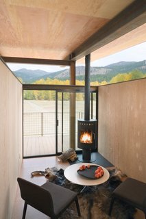 A compact interior with a black fireplace feels simultaneously cozy and boundless, with floor-to-ceiling glass doors that open out to views of the mountains of Washington state. The cork flooring, weathered steel, and wood walls contrast with the raised, open ceiling for the perfect mix of warm and minimalist, open and enclosed.