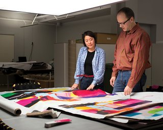 Studio member Eri Shimatsuka (left) and studio manager Petri Juslin (right) compare a first fabric proof to the artist’s original drawing.