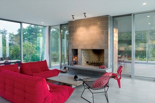 Floor-to-ceiling glass and sliding glass doors create a fluidity between indoors and outdoors, and frame views to the river beyond. The stone-and-brick fireplace acts as a nature-inspired anchor to the otherwise glazed living room.