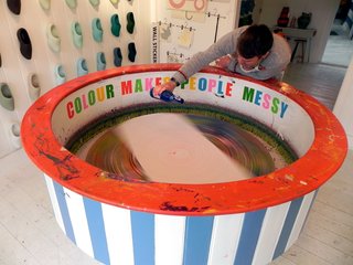 Colour Makes People Happy - Photo 2 of 5 - Currently taking center stage in the shop space is a huge picture painting device which Simon built out of an old potters wheel and an upside down table from Ikea with a drum around the edge. <br><br>A canvas is taped onto the surface of the wheel, when it’s set into motion by the wheel, Simon dribbles thin paint onto the paper to create instant, hypnotic artworks full of swirling hues. Customers are free to create their own artwork, and Simon has also framed a selection that he sells in the shop.