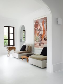 Two pieces from E15’s Shiraz sofa flank the company’s wooden Leila side tables. Hill chose to use flat paint in Benjamin Moore’s Decorators White throughout the home because it emphasizes the chalkiness of the plaster walls, making them "look almost like slate." The sconce shown in the foreground—David Chipperfield’s Corrubedo design for FontanaArte—gives off a soft glow and replaces the dozens of paper-lampshade wall fixtures the owners found in the house when they bought it. Stewart Cohen’s zany photograph of a gun-toting Marfa resident encapsulates Barbara Hill’s offbeat brand of decorating: bright and minimal, yet darkly humorous.