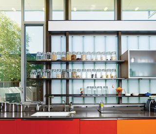 The red- and orange-painted cabinets are meant to reflect sunlight and represent the heart of the home. The glass-fronted cabinets in the kitchen are by Henrybuilt, and the clear containers with dry goods are from the Container Store.