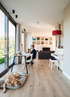 A Modern Take on the Pitched-Roof - Photo 7 of 12 - Bram sits at a table by Gispen in the oak-floored public side of the house, facing the water, while the dog, Bommel, relaxes nearby. "We really like the indoor-outdoor effect," says Bram's dad, Mark de Graaf. "The ground floor opens on three sides—on a summer day, it stays cool."