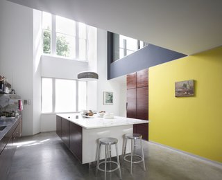Victorian Home in London Gets a Modern Office Addition - Photo 6 of 7 - The kitchen features a concrete island topped with marble. Deja-Vu stools by Naoto Fukasawa surround the island. A print by Guy Gormley, as well as a painting bought during holiday in St. Tropez, hang on the walls.