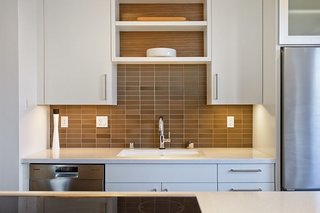 Earth tone tiles back a Kohler sink at this energy efficient home in Davis, California. The backsplash is from Heath Ceramics, the sink is Kohler, and the custom millwork is by Schmidt's Cabinetry.